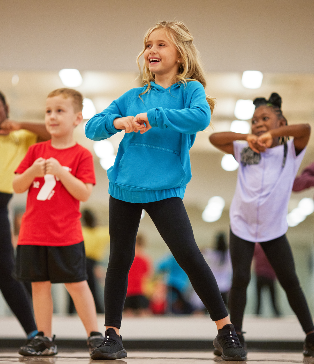 Five young children smile and laugh while practicing their dance routine indoors at the Y youth sports program.
